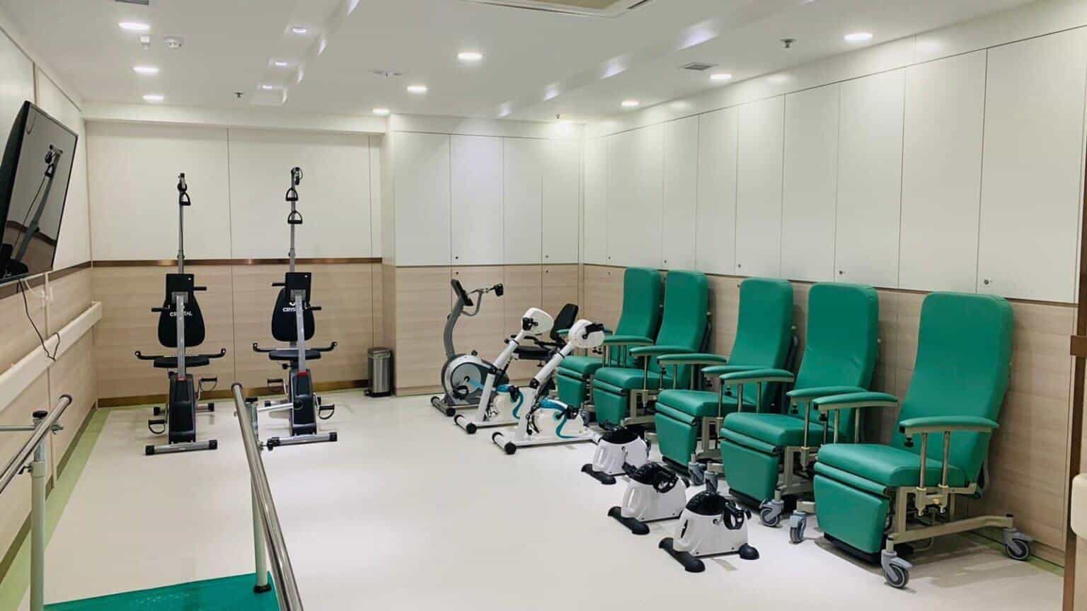 設有扶手步行桿、健身單車、腳踏訓練器及綠色躺椅的室內訓練室